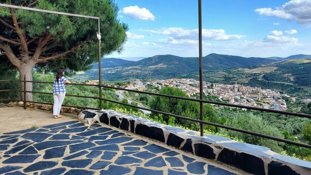 Una terraza empedrada con barandilla metálica que da a una villa y colinas.