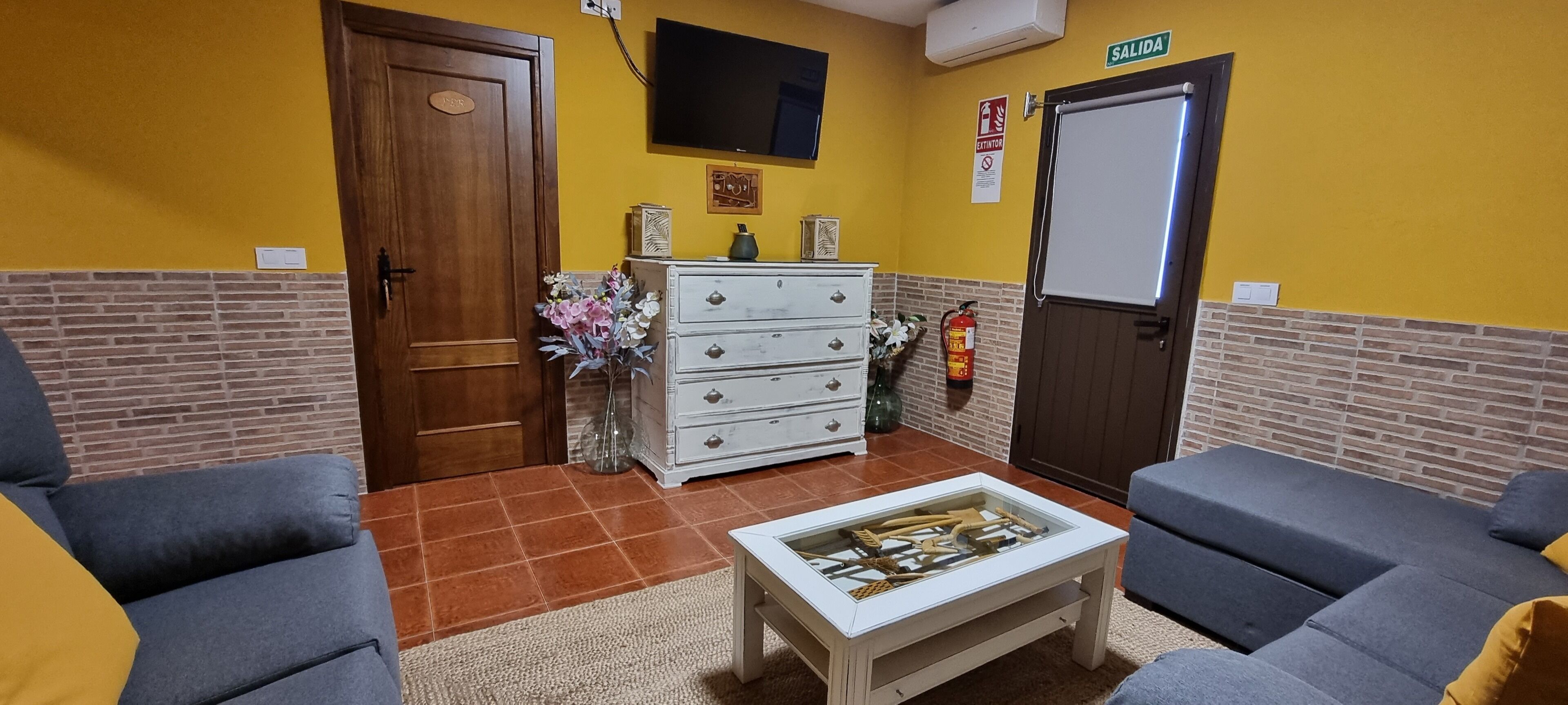 Una habitación con dos sofás, una mesa de centro, un aparador, un televisor, una puerta y un extintor.