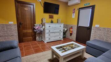 Una habitación con dos sofás, una mesa de centro, un aparador, un televisor, una puerta y un extintor.