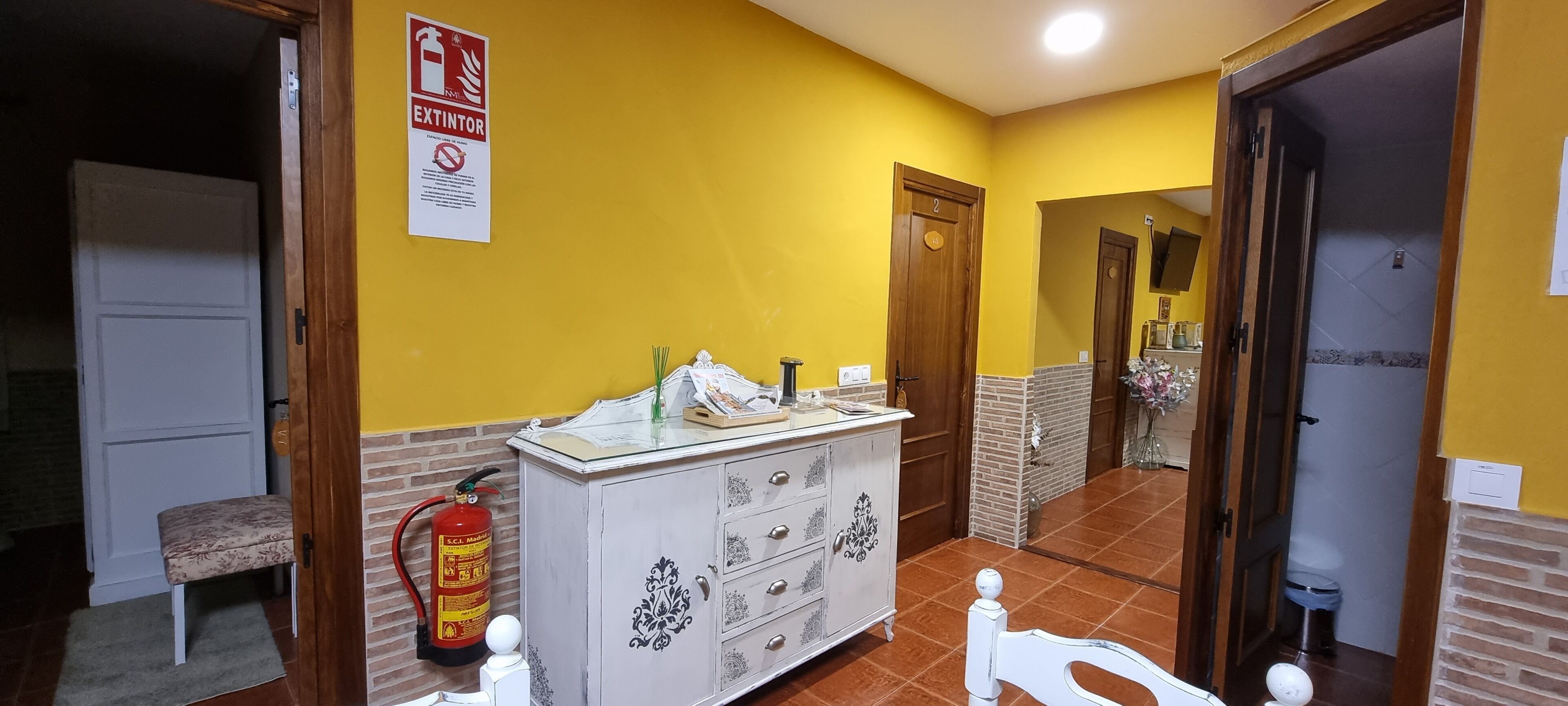 Un baño con paredes amarillas, un mueble blanco, un extintor y un banco.