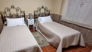 Una habitación con dos camas, cada una con cabecero y mesita de noche con lámpara.