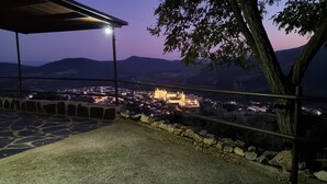 Una terraza empedrada con vistas a un castillo y al pueblo circundante al anochecer.