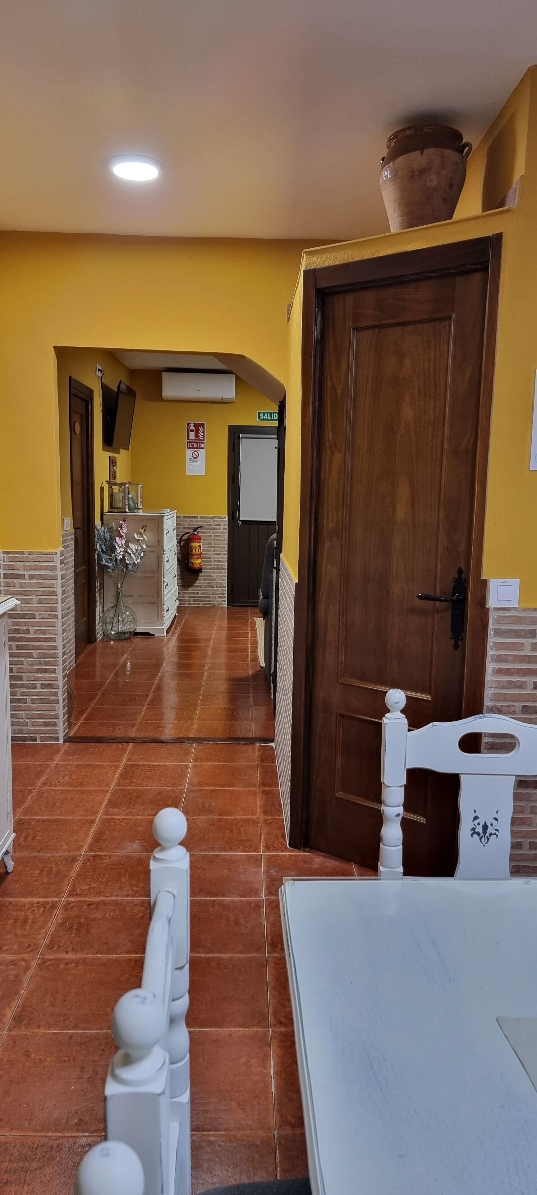 Un pasillo con una puerta de madera, una silla blanca y un suelo de baldosas.