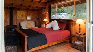 A cozy cabin room with a bed, a fireplace, a window with a view of a car, and a wicker side table.