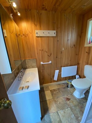 Un bagno con rivestimento in legno, un lavandino bianco, uno specchio, un portasciugamani e un water.
