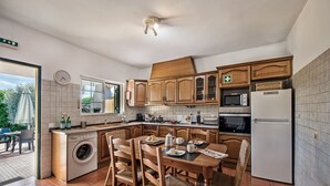 A compact kitchen with wooden cabinets, a built-in washing machine, a dining table with chairs, and a refrigerator. - Rustic Villa with pool near Olhao (Moncarapacho)