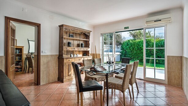A spacious room with a glass dining table surrounded by wicker chairs, a wooden cabinet with shelves, and a large sliding glass door leading to an outdoor area. - Rustic Villa with pool near Olhao (Moncarapacho)