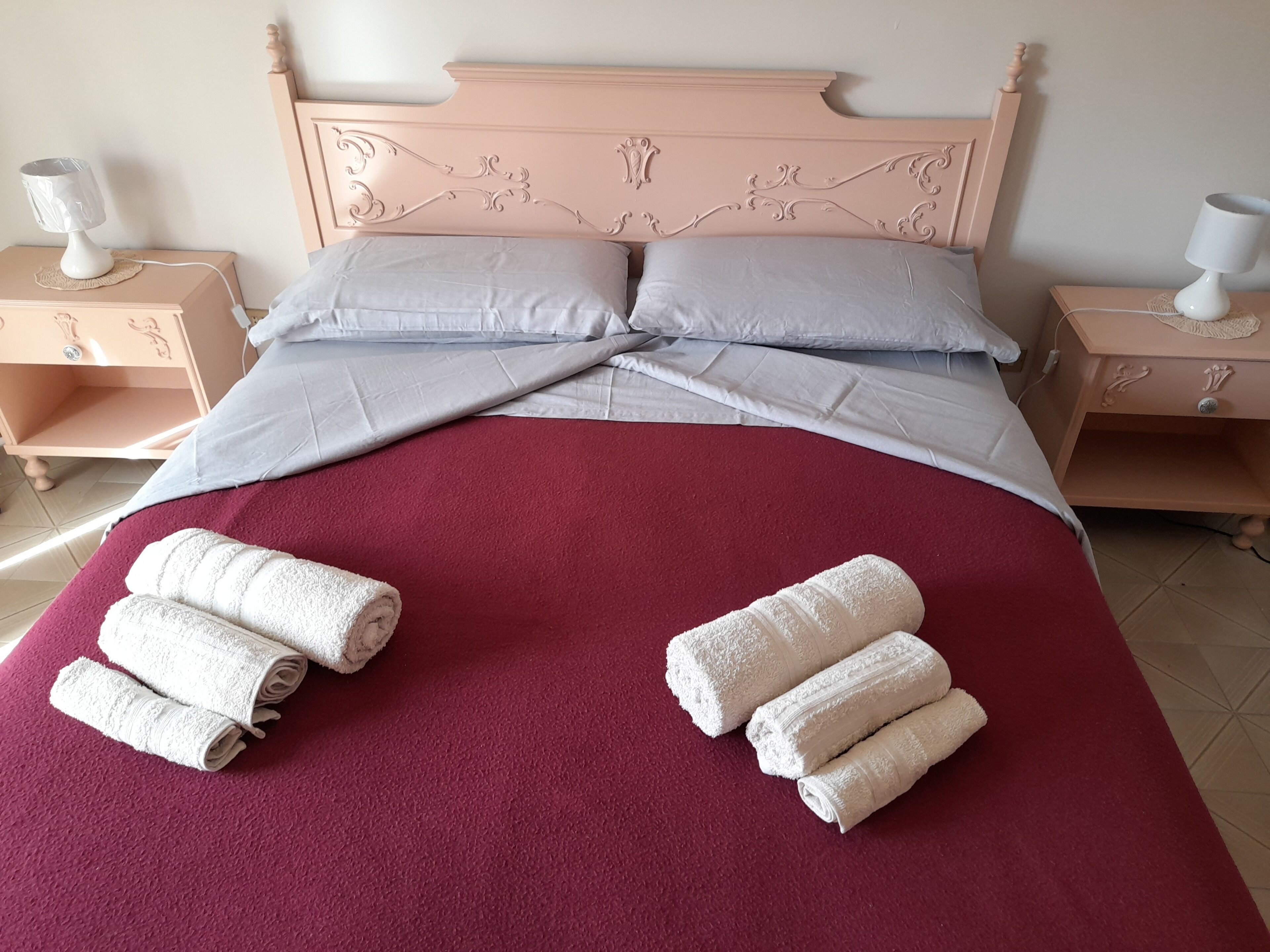 Una cama bien hecha con una colcha roja, dos almohadas y toallas enrolladas sobre la cama.