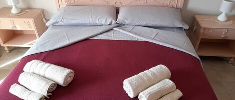 Una cama bien hecha con una colcha roja, dos almohadas y toallas enrolladas sobre la cama.