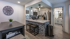 A modern kitchen with a marble island, stainless steel appliances, and a wall clock. - Total Renovation 300' from Chili Express (Angel Fire)