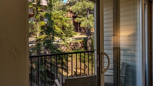 A balcony with a view of a wooded area, a stone wall, and a wooden deck. - Total Renovation 300' from Chili Express (Angel Fire)