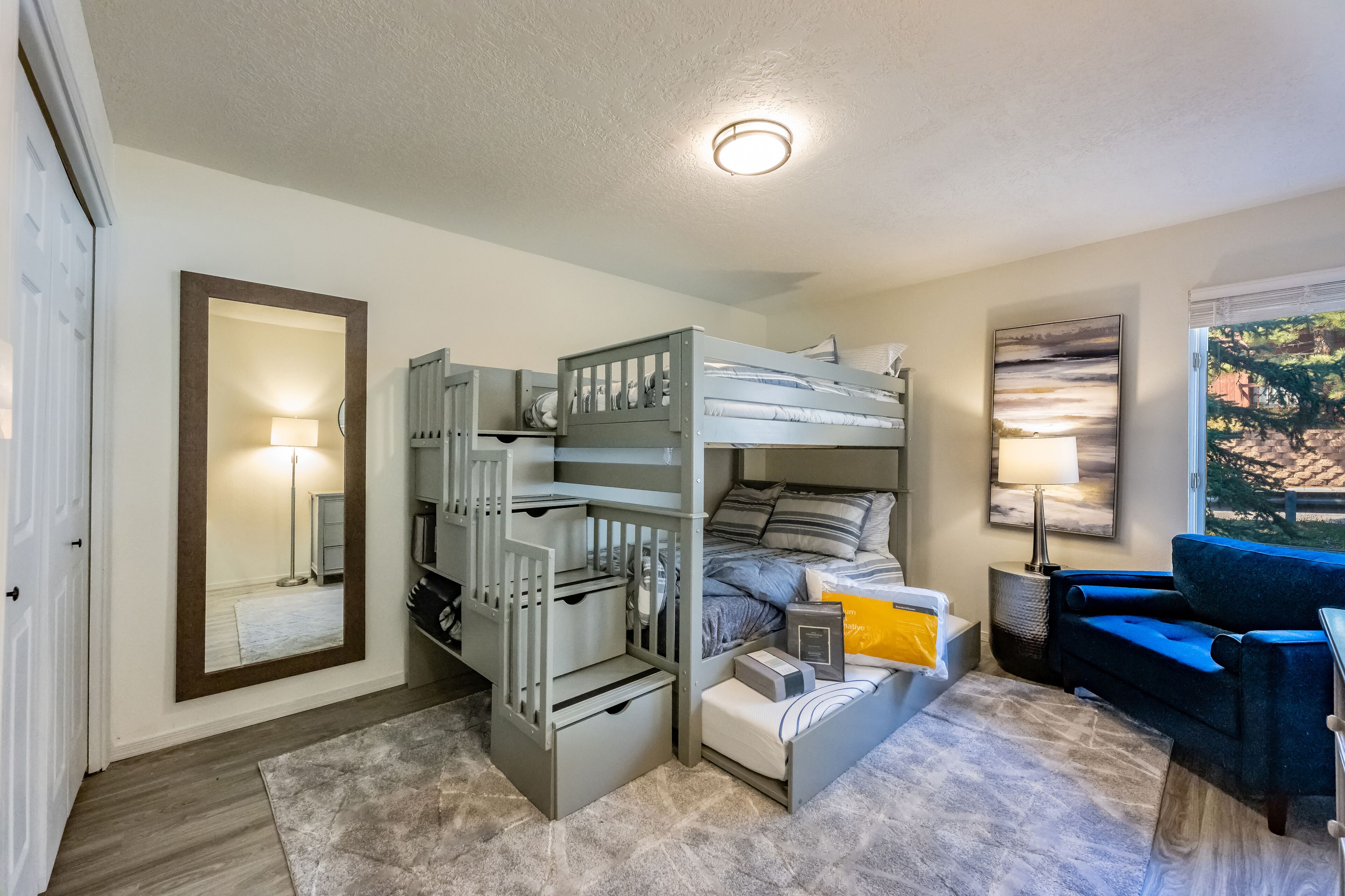 A bedroom with a bunk bed, a desk, a chair, a lamp, and a painting.