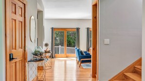 A spacious living area with a wooden floor, a blue sofa, a glass coffee table, and a wooden staircase.