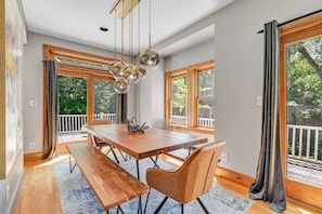 Un grand espace à manger avec une table et des bancs en bois, de grandes fenêtres avec des rideaux et une vue sur une terrasse.