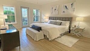 Une chambre avec un grand lit, un bureau et une chaise. Il y a deux fenêtres et un ventilateur de plafond.
