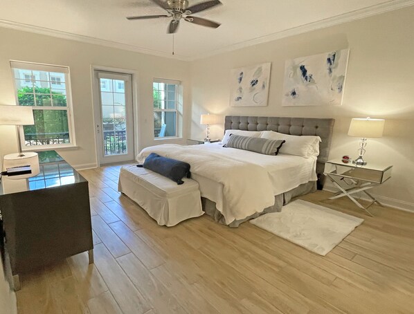 A bedroom with a large bed, a desk, and a chair. There are two windows and a ceiling fan.