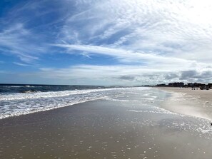 A beach with waves, a clear sky, and buildings in the distance.