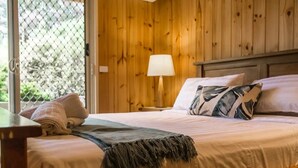 A bedroom with a wooden headboard, a bed with a white and blue bedspread, a gray throw blanket, and a nightstand with a lamp.
