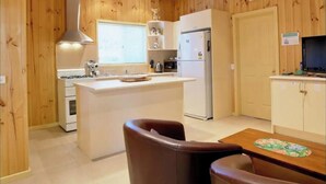 A compact kitchen with wooden paneling, a central island, a refrigerator, a stove, and a dining area with two chairs.