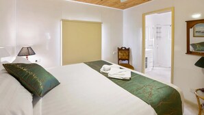 Una habitación de hotel con una cama, una silla, una lámpara y una puerta que da a un baño.