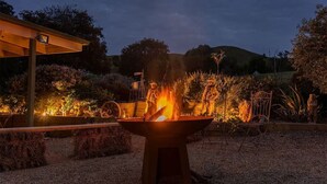 Un hogar con estructura metálica y fuego encendido, rodeado de grava y plantas decorativas.