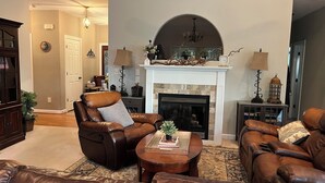 A living room with leather sofas, a fireplace, and a chandelier. - Island home on the water with pool.  Bring your boat or jet skis ! Golf near by (Currituck)