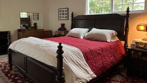 A bedroom with a large bed, a dresser, a nightstand, a lamp, and a window with a view of trees. - ♥️ of UofO pristine residence for the World Championships (Eugene)