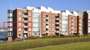 Ein modernes Mehrfamilienhaus mit mehreren Balkonen, einem gepflegten Rasen und freiem Blick auf das Meer.