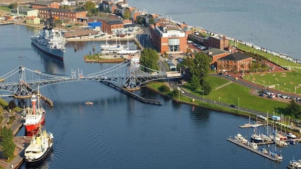 Ein Hafen mit einem großen Schiff, einer Brücke und Gebäuden, darunter ein markantes Gebäude aus roten Ziegeln.