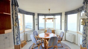 Ein Essbereich mit einem runden Tisch, sechs Stühlen und Meerblick durch große Fenster.