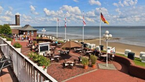 Eine Terrasse am Meer mit Sitzgelegenheiten im Freien, einem Glockenturm und Flaggen.