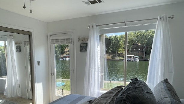 Une chambre avec une grande fenêtre donnant sur un lac, un lit avec une literie aux couleurs sombres et une porte menant à l’extérieur.