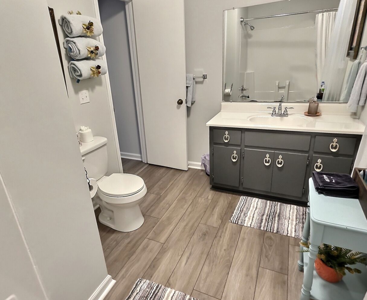 A bathroom with a toilet, sink, mirror, and dark cabinets.