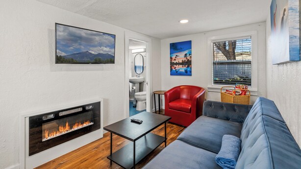 A modern living room with a fireplace, a sofa, a red chair, and artwork on the walls. - Downtown Big Sky Bungalow w/AC, Fully Fenced Yard, W/D, 2 Smart TVs, Speedy WiFi (Flagstaff)