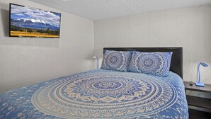 A bedroom with a bed, a wall-mounted TV, and a bedside table with a lamp. - Downtown Big Sky Bungalow w/AC, Fully Fenced Yard, W/D, 2 Smart TVs, Speedy WiFi (Flagstaff)