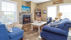 A living room with a fireplace, blue furniture, a bookshelf, and a painting of a beach scene. - Sea Breeze Manor (Port St. Joe)