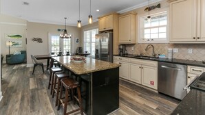 A modern kitchen with a central island, stainless steel appliances, and a dining area with bar stools. - Veranda Views (Port St. Joe)