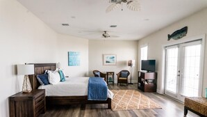 A bedroom with a bed, nightstand, lamp, chair, TV, and a view of the outdoors. - Veranda Views (Port St. Joe)