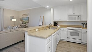 Een moderne keuken met witte kasten, een ingebouwde magnetron en een fornuis. Er is een beige aanrecht en een houten vloer.