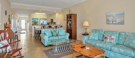 A living room with a sofa, coffee table, and rocking chairs. There is a kitchen in the background.