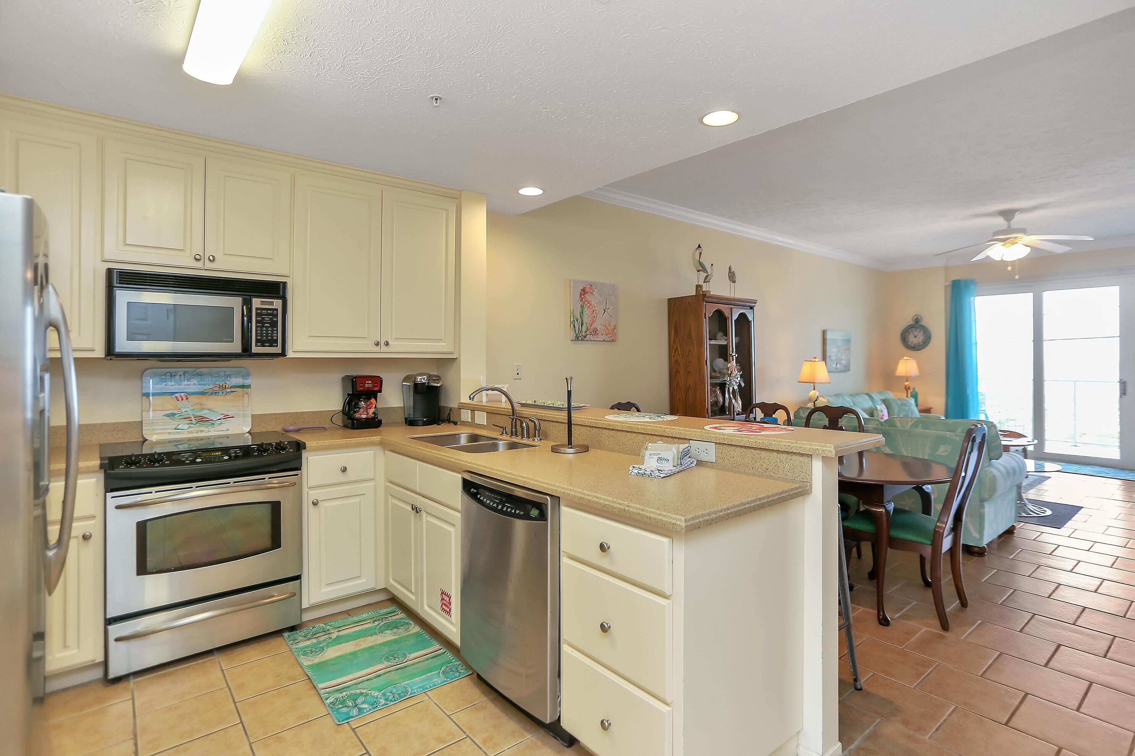 A kitchen with white cabinets, stainless steel appliances, a dishwasher, and a dining area with a table and chairs.