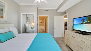 Une chambre à coucher avec un lit, une télévision, un ventilateur de plafond et une vue sur la plage par la fenêtre.