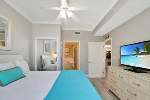 Un dormitorio con cama, televisor, ventilador de techo y vista a la playa a través de la ventana.