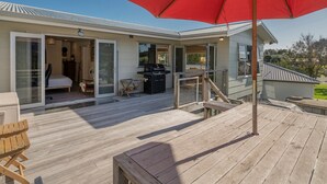 Eine Terrasse mit einem roten Sonnenschirm, einem Grill und einer Liege.