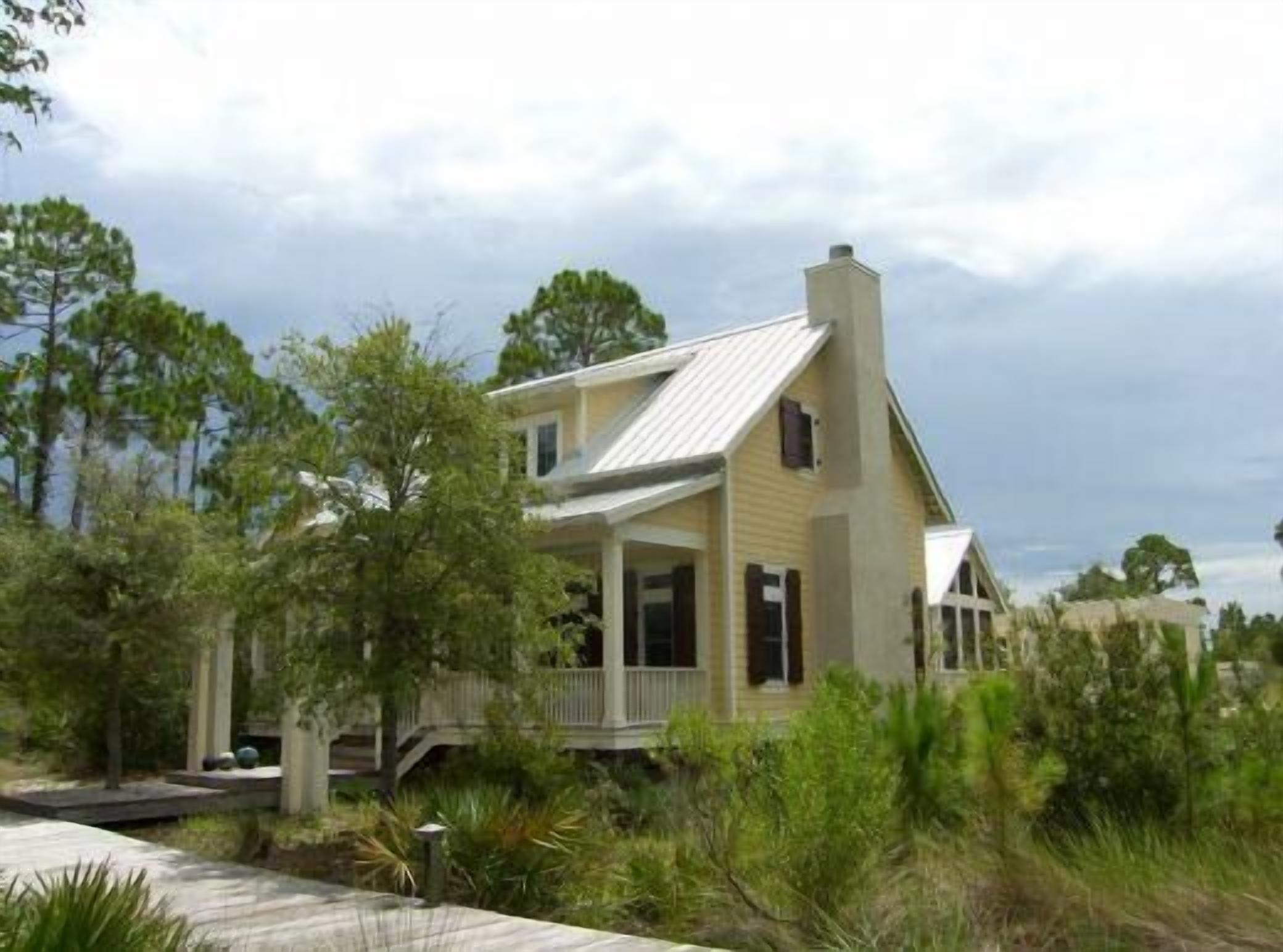 A two-story house with a porch and a chimney, surrounded by trees and vegetation.