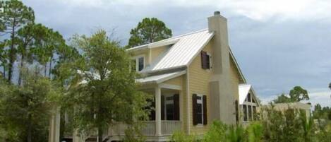 A two-story house with a porch and a chimney, surrounded by trees and vegetation.