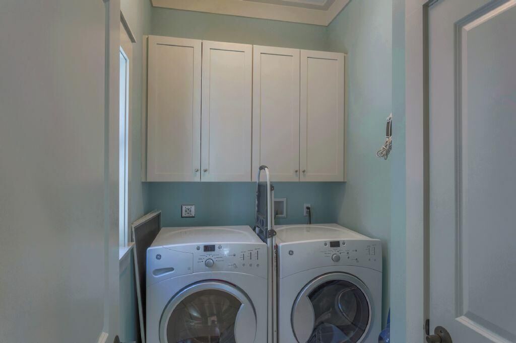 A laundry room with two front-loading washing machines and a set of white cabinets above them.
