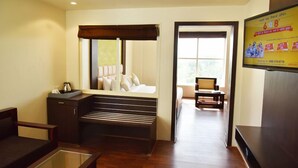 A hotel room with a bed, a seating area with a bench, a small table, and a TV mounted on the wall. - Rester Select Jodhpur (Jodhpur)