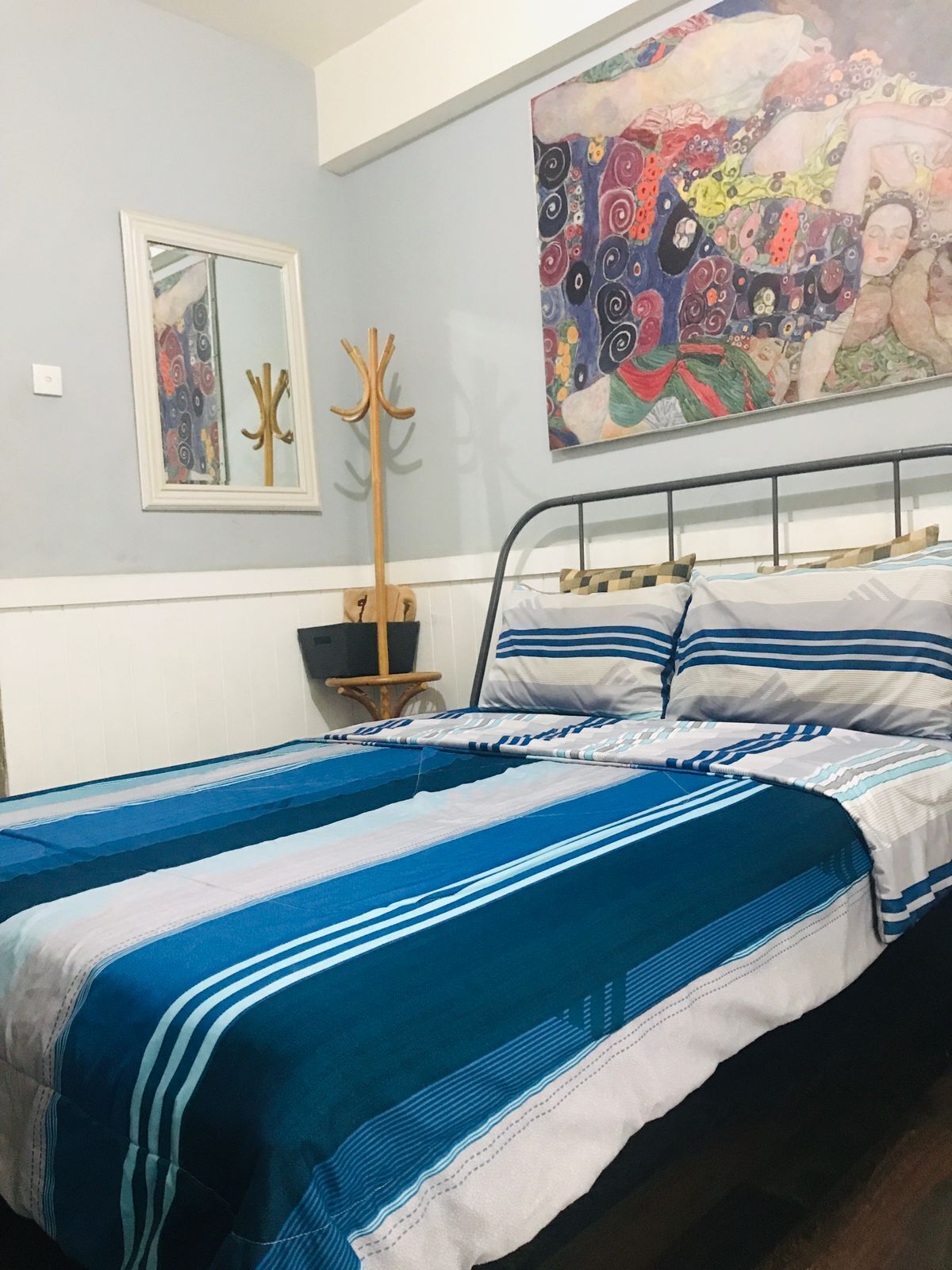 Ein Schlafzimmer mit zwei Betten, einem großen abstrakten Gemälde, einem Kleiderständer und einem Spiegel.