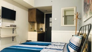 Ein Schlafzimmer mit Bett, einem an der Wand befestigten Fernseher, einer Küchenzeile und einer Tür zu einem anderen Raum.